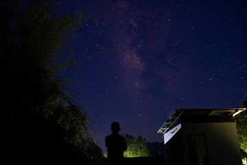 Fototapeta na wymiar Boy standing in front of milkyway on roof slab of house