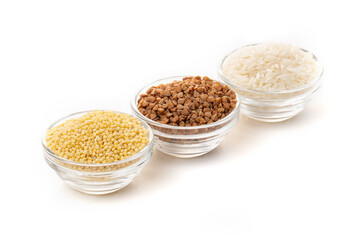 Three transparent bowls with buckwheat, millet, and white rice grains isolated on a white background.