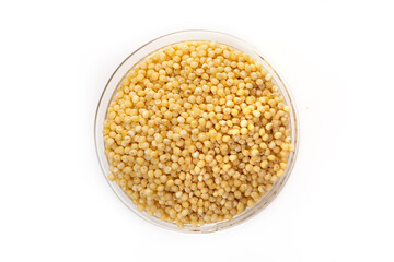 Raw yellow millet in a transparent glass plate on a white background. Top view.