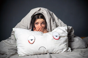Girl hugs a pillow with tired red eyes and a sad expression on her face, hides under the covers....
