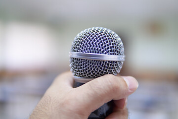    Hands holding a microphone in a conference room.                                                  