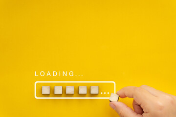 Loading, hand putting wood cube in progress bar. Loading bar on bright yellow background