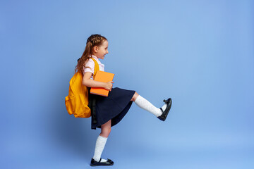 Cute happy kid in uniform. raises his leg high and runs on purple background. child with backpack. little girl is ready for school. Dynamic images that go back to conceptual school. holidays begin.