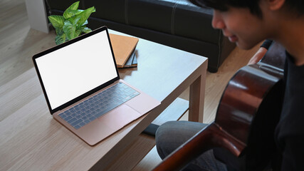 Young man playing guitar and using laptop computer.