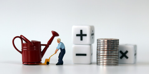 A miniature man carrying a red watering can with a handcart ​and a white cube with arithmetic...