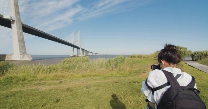 Young woman captures a moment and takes a photo of the scenery. Urban and nature. Female photographer takes a photo of Vasco da Gama bridge.