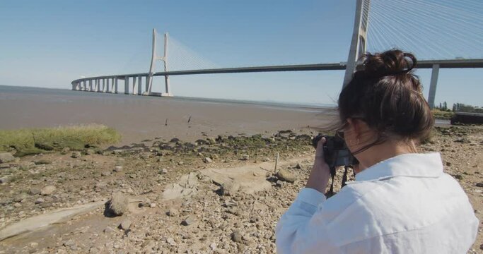 Young woman taking a photo of the Tagus river and Vasco da Gama bridge in Lisbon, Portugal.