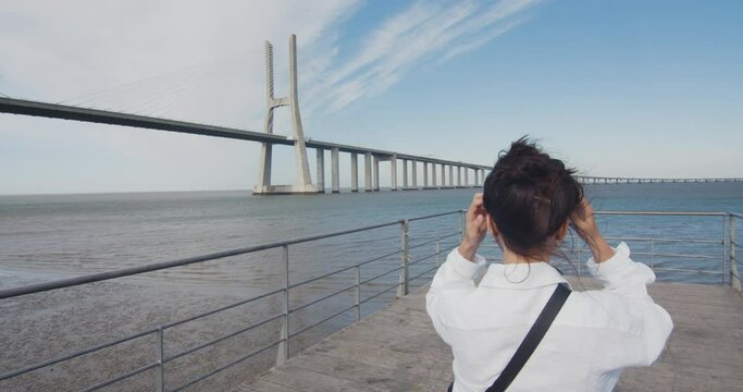 Free young woman walks in the pier, by the river, and enjoys the amazing view. Vasco da Gama bridge (Lisbon, Portugal). Wonder and awe in solitude