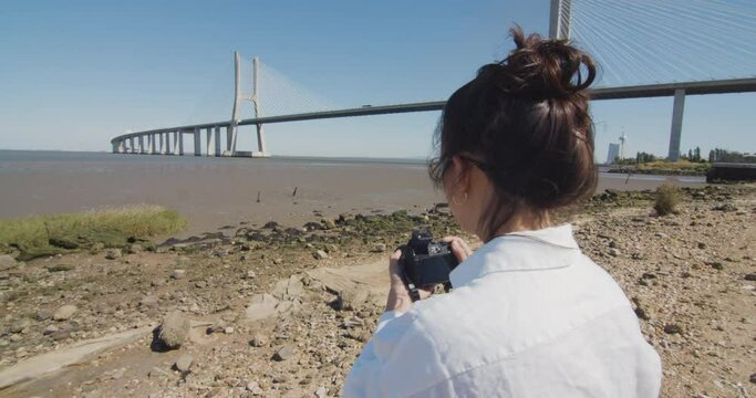 Young woman taking a photo of the Tagus river and Vasco da Gama bridge in Lisbon, Portugal.