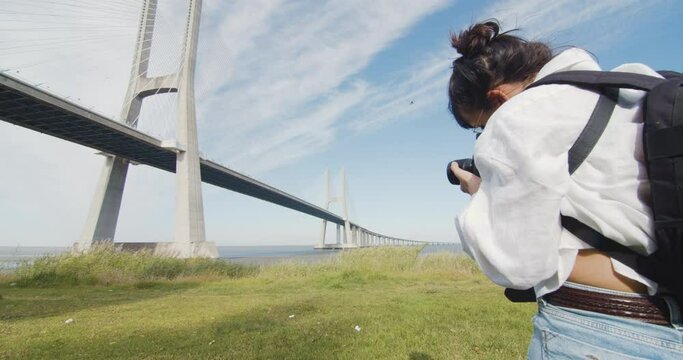 Young woman takes a photo of the scenery. Urban and nature. Female photographer takes a photo of Vasco da Gama bridge in Lisbon, Portugal