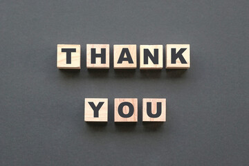 Thank you alphabet letters on wooden blocks on dark grey background. Top view.