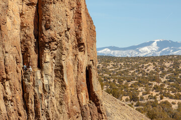 Rock climbers rest on a distant rock wall in Diablo Canyon, between Los Alamos and Santa Fe New Mexico, with the Sangre de Cristo Mountains in the background. 