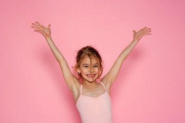 Happy little girl with hands up portrait on a pink background. Space for text.