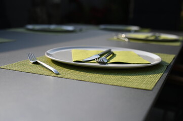 gedeckter grauer Tisch mit weissen runden tellern und gr&uuml;nen servietten und unterlage mit metall besteck messer und gabel 