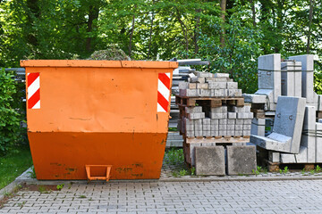 Orange industrial transportable dumpster container and cobble stones on palette at construction site