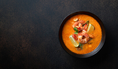 Tom Yum kung Spicy Thai soup with shrimp in a black bowl on a dark stone background, top view, copy...