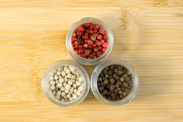 Spices, white, black and red peppers in small glass jars on bamboo wood background, close-up