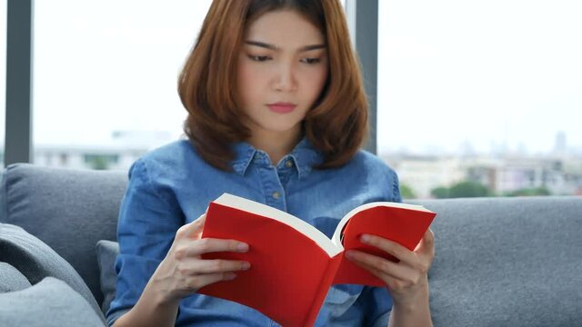 Relax asian woman reading book sitting on sofa in living room holding book to read. Young woman relaxation reader reading open book leisure mind. Happiness beauty woman person smiling face happy time