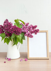 Bouquet of lilac flowers in a vase and empty wooden frame