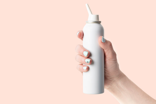 spray bottle with salt sea water for nasal cavity hygiene in female hand isolated on pink background