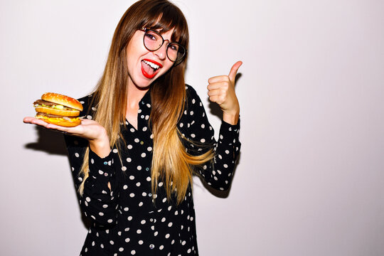 Indoor bright flash image of woman eating big junky burger,