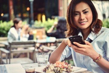Asian woman smiling while playing on her phone in an outdoor cafe. face focus