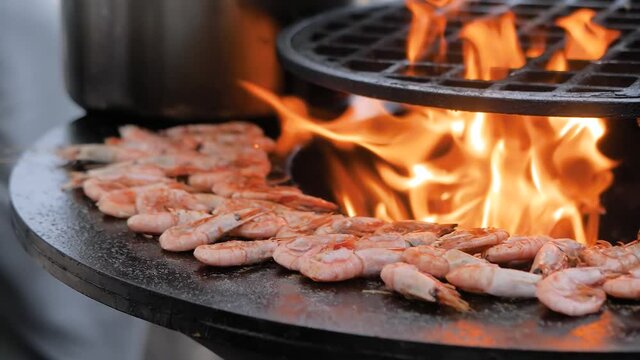 Slow motion: process of grilling fresh red king prawns on brazier with hot flame at summer local food market - close up view. Outdoor cooking, gastronomy, seafood, barbecue, street food concept