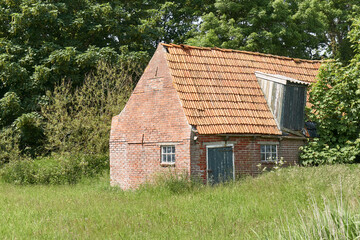 Fototapeta na wymiar Old decaying shed with red bricks and orange tiles near Ferwert in The Netherlands. 