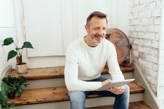 Attractive middle-aged man relaxing on loft steps with a tablet
