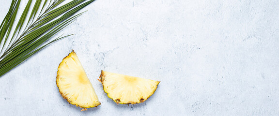 Pineapple slices and palm leaf on a concrete background. Top view, flat lay. Banner