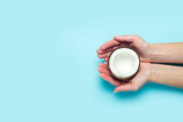 Female palms hold an open half of a coconut on a blue background. Top view, flat lay