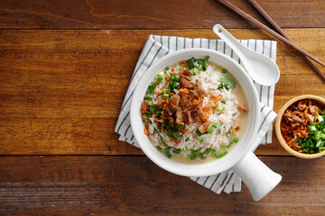 Porridge with spiced pork porridge Garnish with spring onions, coriander, sauteed cabbage, and fried garlic in a baking cup with handle on a wooden table.