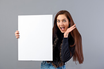 emotional young teenager woman showing blank signboard with copy space, isolated on gray