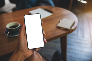Mockup image of a man holding black mobile phone with blank white screen in cafe