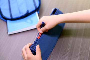 Child's hand closing a zipper of a pencil case. On the table is a blue backpack with a notebook. Back to school concept. © Silvia 