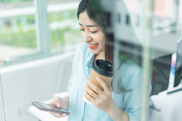 Portrait of happy young businesswoman using her phone by the glass door