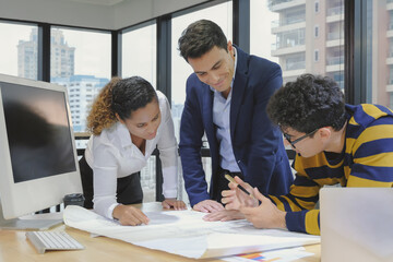 Young caucasian male manager happy smiling face meeting with multi ethnic designer team staff on mockup blueprint paper at office desk space. Selective focus.