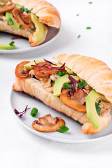 Croissant sandwich with scrambled eggs, roasted mushrooms, avocado and cream cheese on the white table