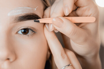 Master with tweezers and wax depilation of eyebrow hair in women, brow correction - obrazy, fototapety, plakaty