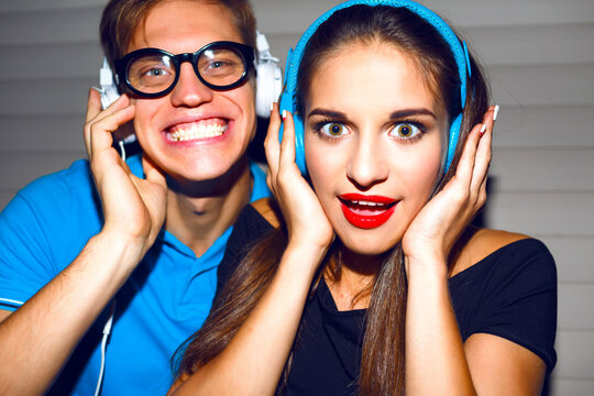 Close up portrait of pretty crazy couple  having fun at night student part, funny emotions, hipster style bright makeup, listening music at earphones, bright outfits, night image with flash.