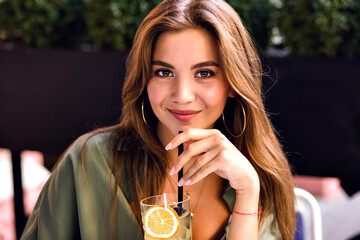 Young pretty woman drinking tasty sweet cocktail at city terrace