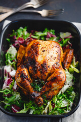 .Top view of whole roasted chicken with fresh salad in black dish.