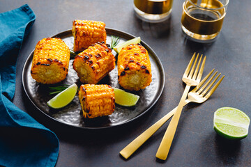 Roasted or grill corn cob with olive oil and salt on a black plate.