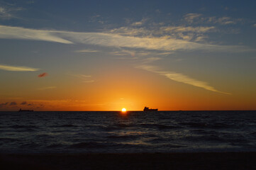 Naklejka na ściany i meble Beautiful Orange Sun rising above the sea level on Fort Lauderdale Beach with fishing boat far away