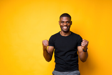 Happy african american man rejoices in victory clenching his hands into fists and smiling broadly