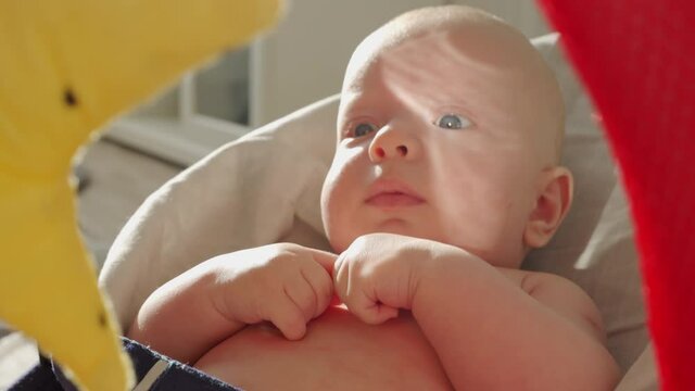 Baby face in sunlight, cute three month old baby boy rocking himself while sitting in rocking chair in front of toy mirror. High quality 4k footage