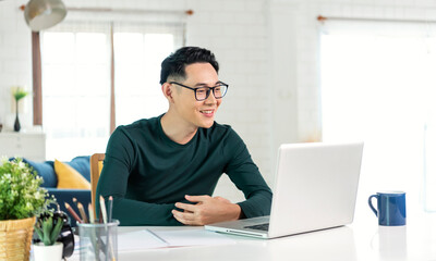 Fototapeta na wymiar Smiling handsome asian businessman working remotely from home. He is webinar video conference..