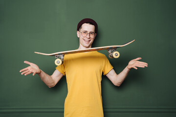 Portrait of young fashionable hipster man posing over green wall background. Caucasian male holding skateboard and smiling