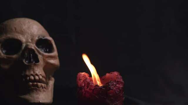 The candle burns and goes out on a black background and a blurry image of a skull