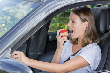 woman driving a car about to bite into an apple